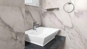 Un baño con un lavamanos blanco, un espejo, un perchero para toallas y un interruptor de luz en la pared.