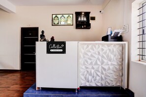 A reception desk with a sign indicating it's company-serviced, a statue, and framed religious artwork on the wall. - Collection O Sunset Point PB Road (Hubli)