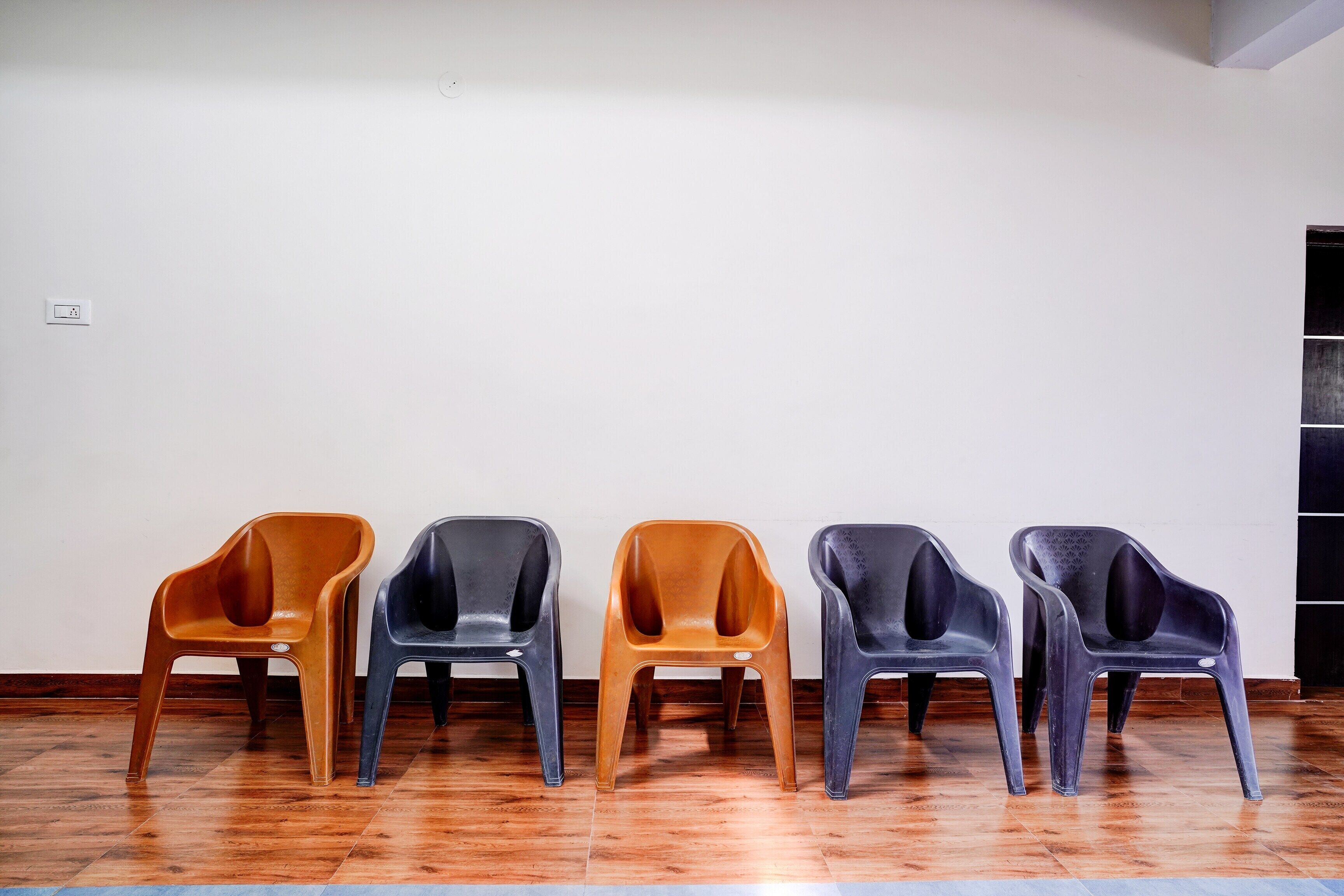 A row of five chairs in a room with wooden flooring and a white wall.