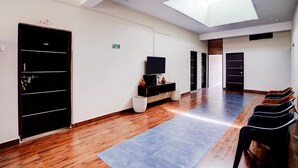 Habitación de hotel con tragaluz, televisor, una pequeña mesa con objetos decorativos, perchero con zapatos y una puerta con la etiqueta '106'.