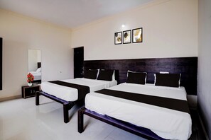 A hotel room with two beds, a bedside table with a vase of flowers, a mirror, and three framed pictures on the wall. - Collection O Sunset Point PB Road (Hubli)