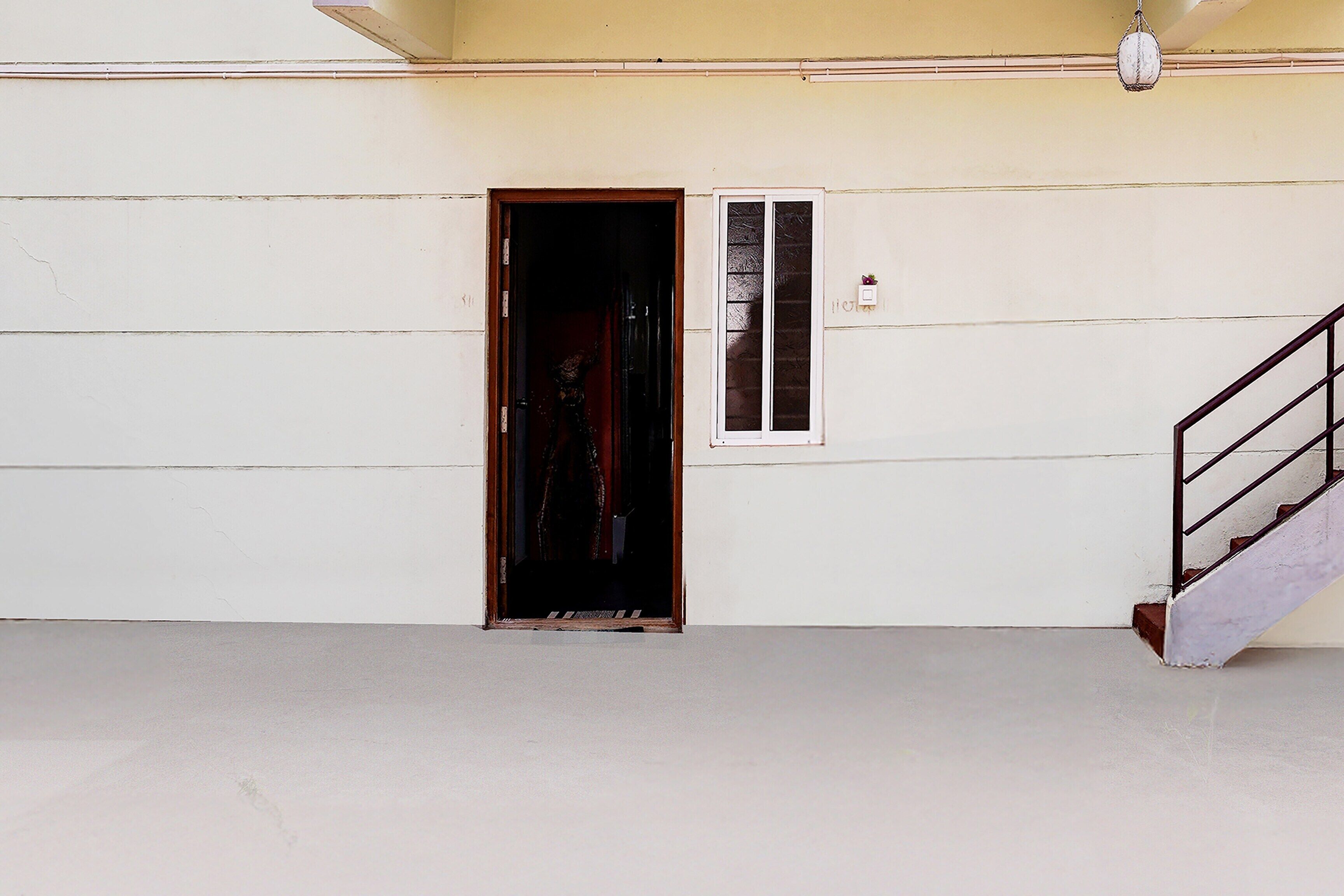Una puerta que da a un interior oscuro, una ventana pequeña con persianas y una escalera con barandilla de metal.