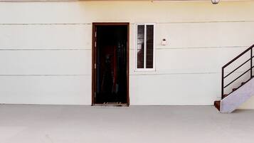Una puerta que da a un interior oscuro, una ventana pequeña con persianas y una escalera con barandilla de metal.