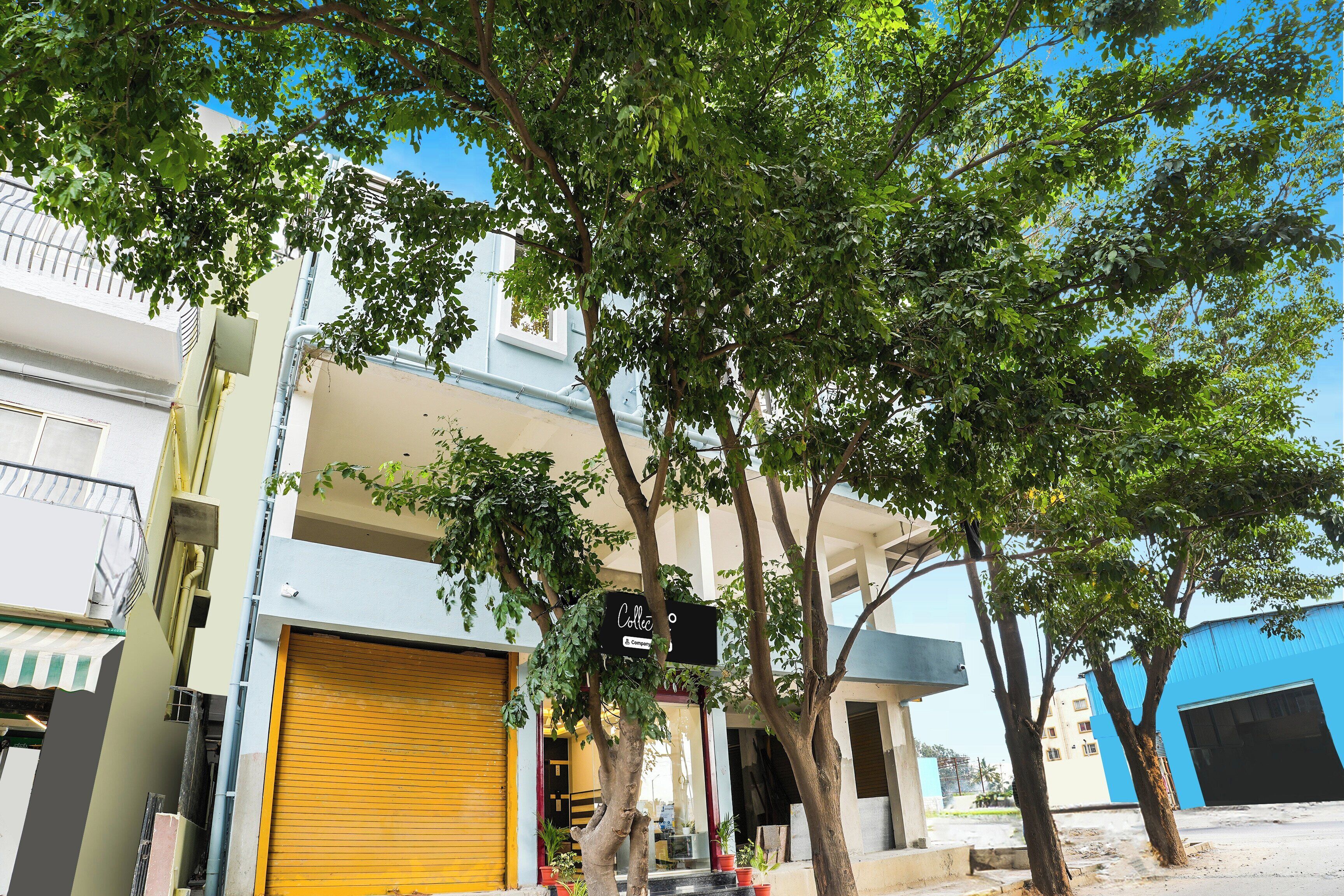 A building with a closed yellow shutter, a signboard, and a tree in front.