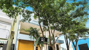 Un edificio con una persiana amarilla cerrada, un letrero y un árbol en frente.