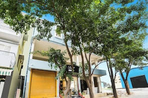 Un edificio con una persiana amarilla cerrada, un letrero y un árbol en frente.