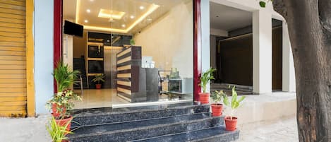 Entrada moderna de un edificio con puerta de vidrio, una escalera que sube y plantas en macetas en los escalones.