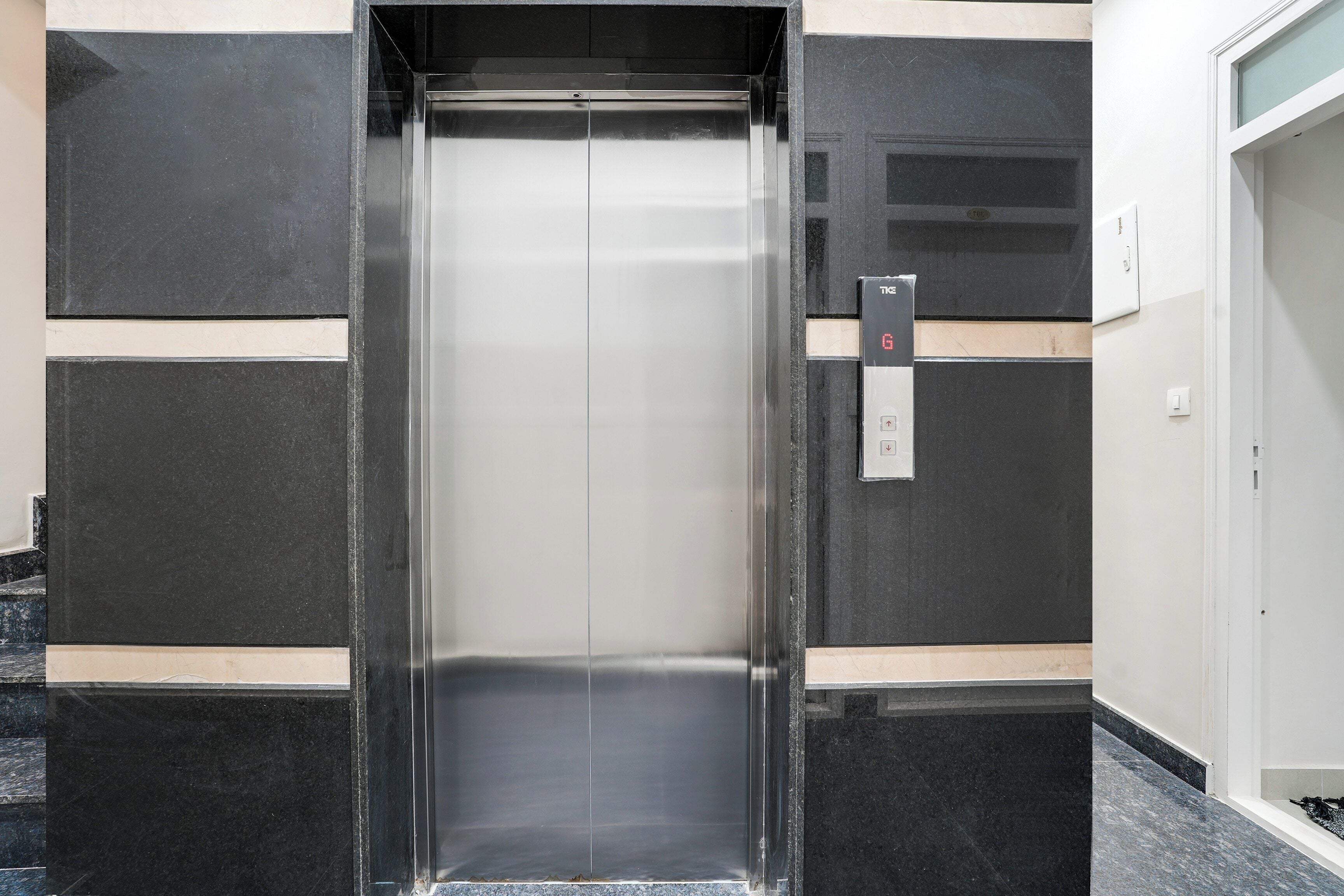 An elevator with a metallic finish, a control panel with a digital display, and a wall with a geometric pattern.