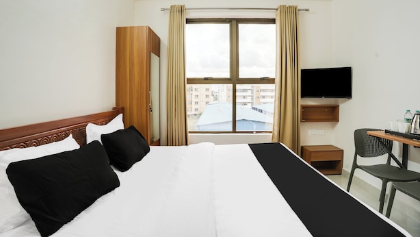 Una habitación de hotel con cama, escritorio, silla, televisión y ventana con cortinas.