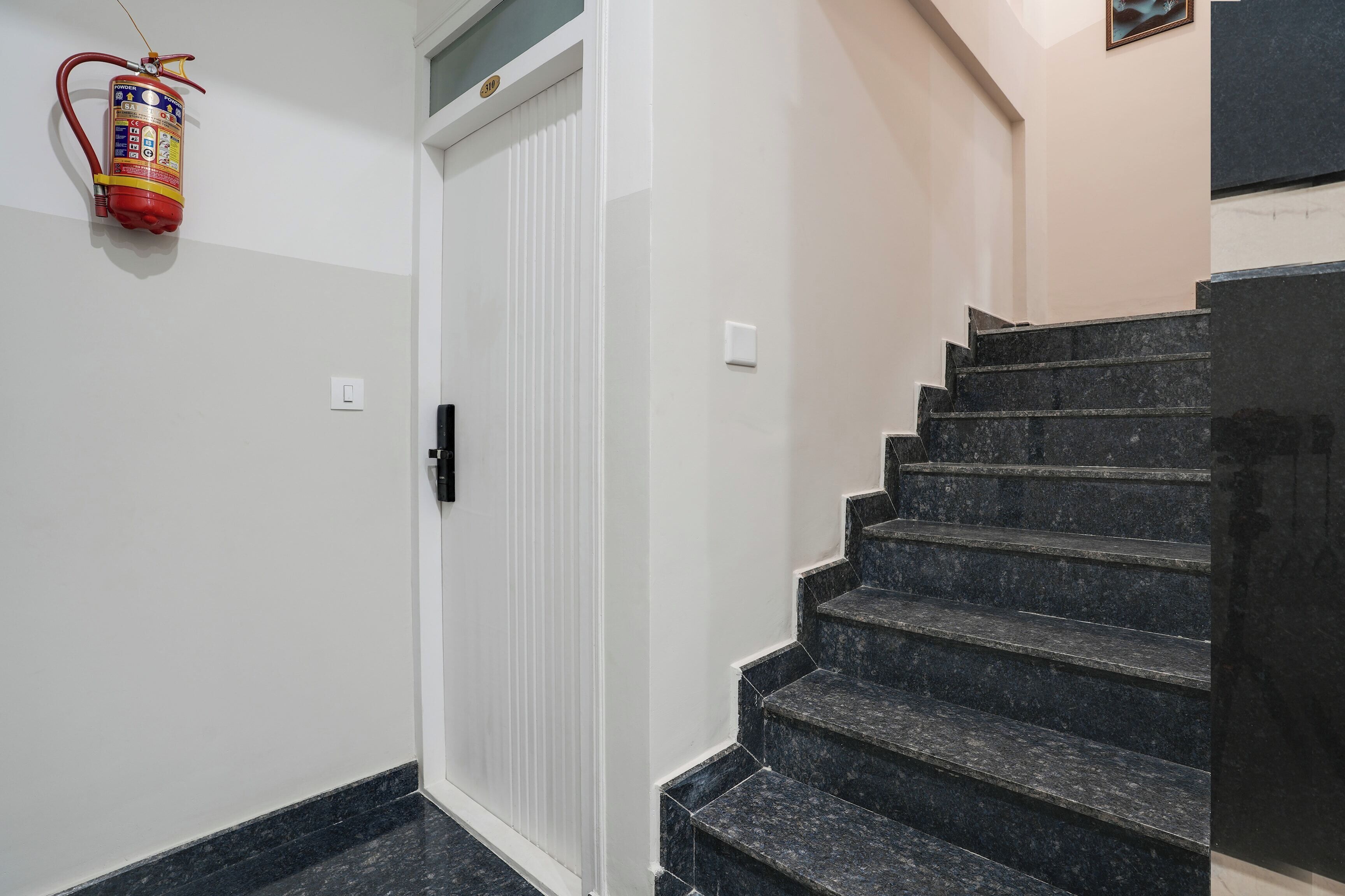 Una escalera con peldaños negros que conduce a una puerta, sobre la cual se encuentra un extintor de incendios.
