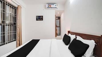 Habitación de hotel con cama, ventana con barrotes, equipo de aire acondicionado y un cuadro en la pared.