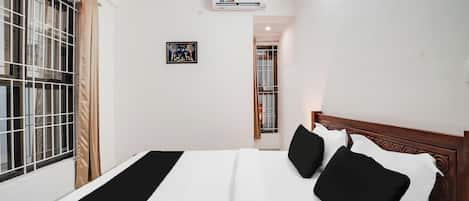A hotel room with a bed, a window with metal bars, an air conditioning unit, and a framed picture on the wall.