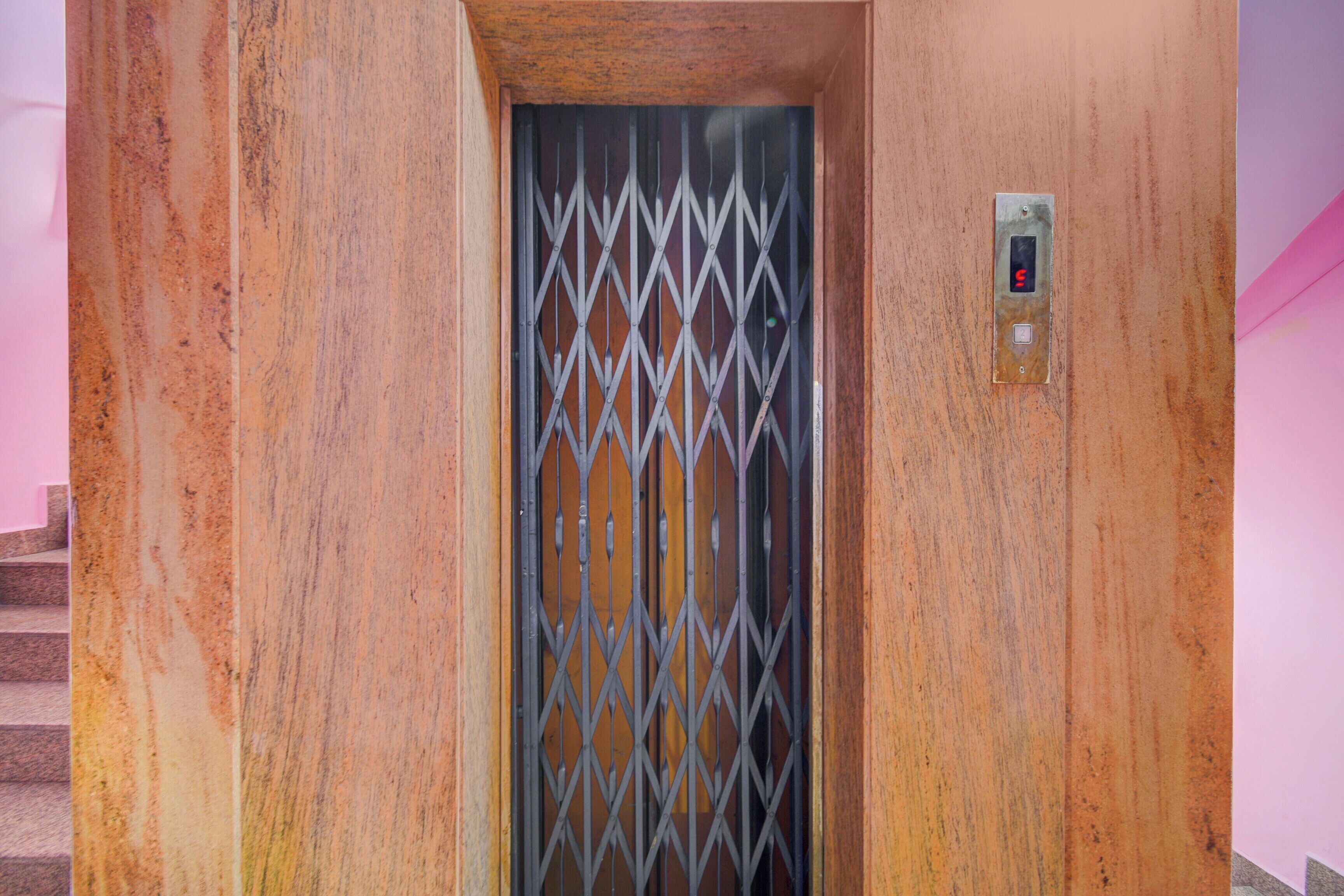 An elevator with a metal grid door, a control panel with a red button, and a staircase to the left.