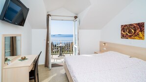 A hotel room with a bed, a desk, a chair, a television, and a balcony with a view of the sea. - Villa Samba - Standard One-bedroom Apartment With Balcony and Sea View (Zupa dubrovacka)