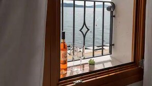 Ett fönster med utsikt över havet och en flaska sprit på fönsterbrädan.