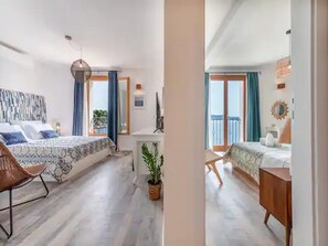A bedroom with a bed, a desk, a chair, and a balcony.