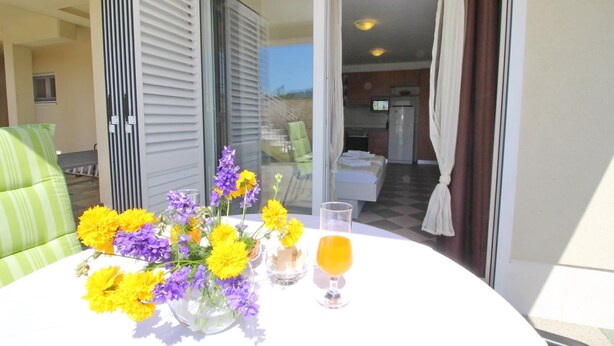 Ein Balkon mit Tisch für zwei Personen, eine Blumenvase und ein Glas Orangensaft.