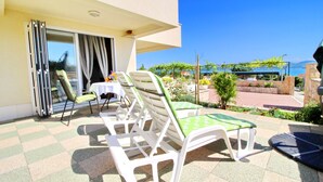 Eine Terrasse mit Sitzgelegenheit im Freien, ein Tisch mit Blumen und Blick auf das Meer und die Berge.