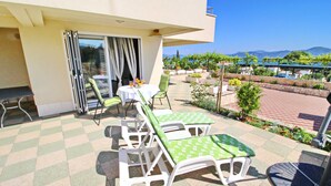 Eine Terrasse mit Tisch und Stühlen, Blick aufs Meer und ein Garten mit verschiedenen Pflanzen.