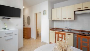 A compact kitchen with white cabinets, a wooden dining table, and a television mounted on the wall. - Apartment Bella Vista - Two Bedroom Apartment With Terrace (Marina)