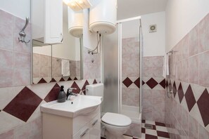 Ein Badezimmer mit Dusche, Toilette, Waschbecken und Spiegel.