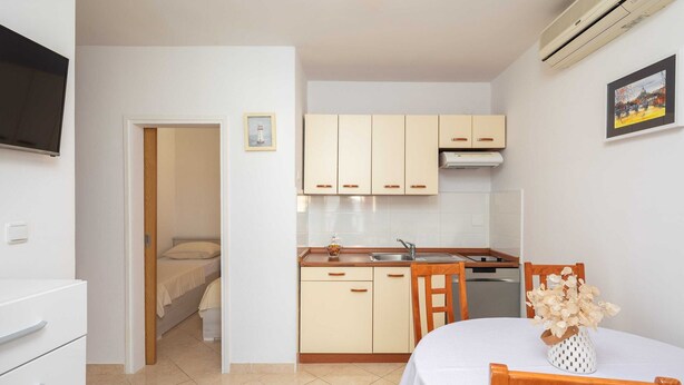 A compact kitchen with white cabinets, a dining table with chairs, and a TV mounted on the wall. - Apartment Bella Vista - Two Bedroom Apartment With Terrace (Marina)