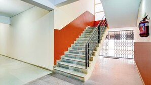 Eine Treppe mit Metallgeländer, ein an der Wand befestigter Feuerlöscher und ein Blick auf einen Parkplatz durch ein Metallgitter.
