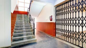 A staircase with a metal railing leading to a landing, a fire extinguisher mounted on the wall, and a decorative metal gate.