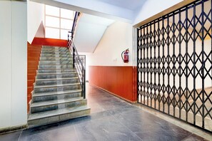 A staircase with a metal railing leading to a landing, a fire extinguisher mounted on the wall, and a decorative metal gate. - Collection O Electronic City (Anekal)