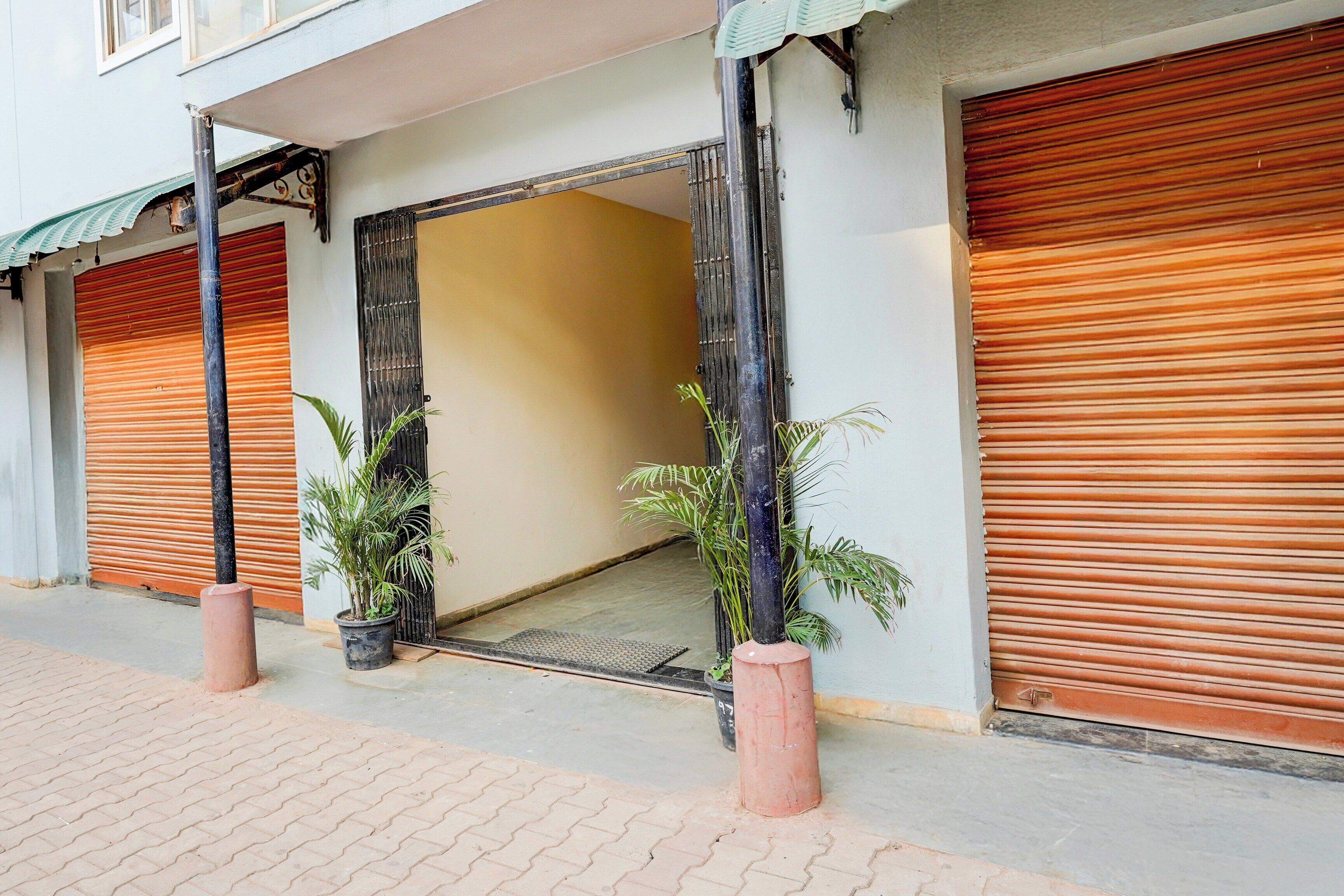 A building with closed shutters, potted plants, and a visible entrance.