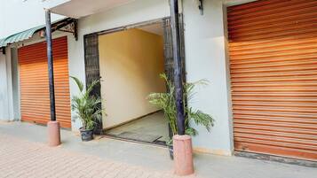 A building with closed shutters, potted plants, and a visible entrance.