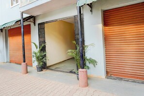 A building with closed shutters, potted plants, and a visible entrance. - Collection O Electronic City (Anekal)
