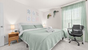 Ein ordentlich eingerichtetes Schlafzimmer mit Bett, Nachttisch, Lampe und Schreibtisch mit Stuhl.