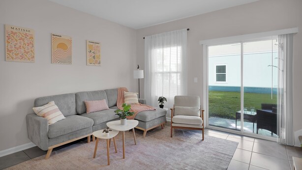 Ein modernes Wohnzimmer mit einem grauen Sofa, einem weißen Sessel und einem kleinen runden Tisch. Zwei Bilder hängen an der Wand, und ein großes Fenster bietet einen Blick ins Freie.