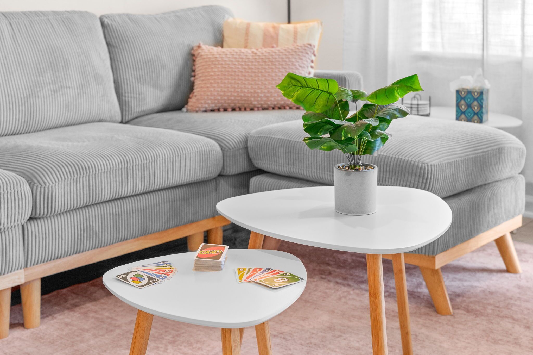 Ein Wohnzimmer mit grauem Sofa, einem weißen Couchtisch und einem kleinen Beistelltisch mit Spielkarten.
