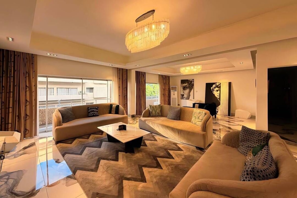 Una sala de estar moderna con candelabro, sofás, una mesa de centro y un ventanal grande.