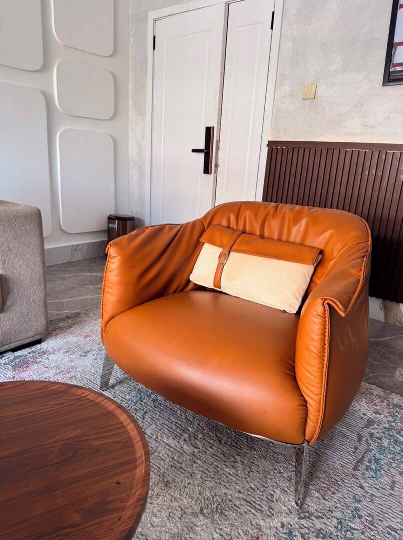 A room with a brown leather armchair, a round wooden table, and a white door.