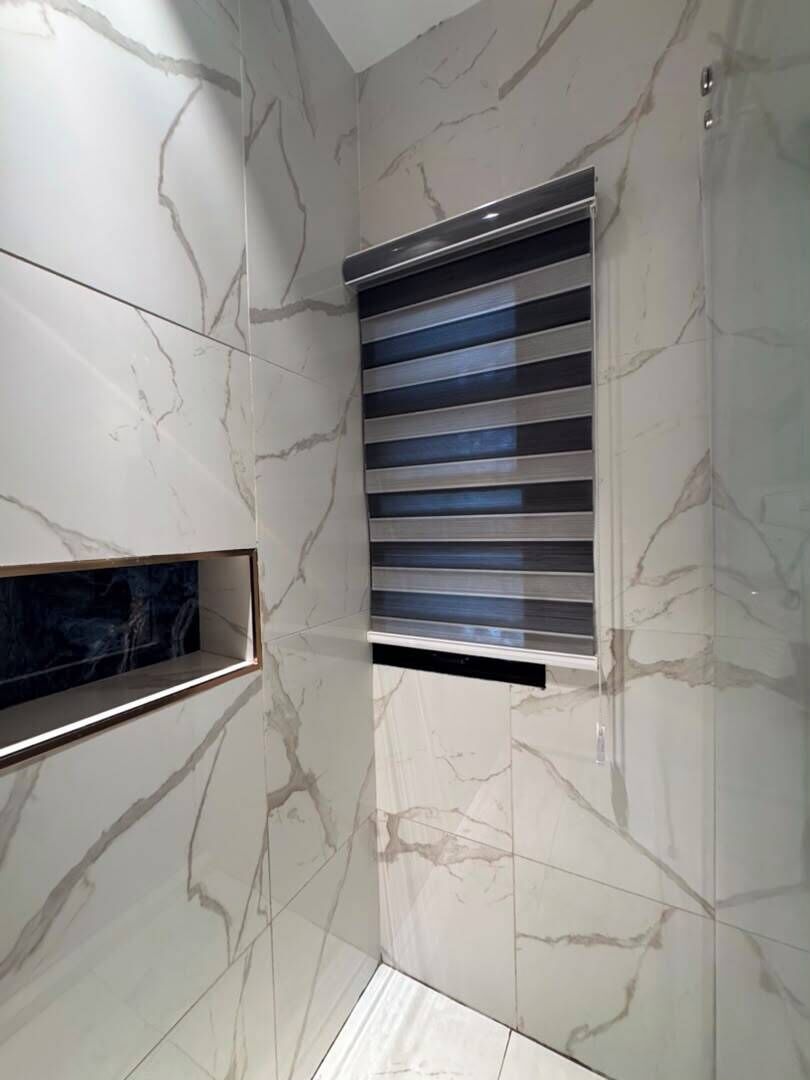 A bathroom with marble walls, a built-in shelf, and a ventilation grille.