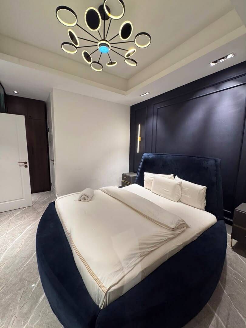 A modern bedroom with a round bed, a dark headboard, and a unique ceiling light fixture.