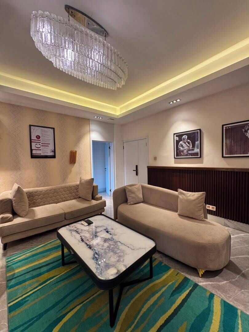 A modern living room with two sofas, a marble coffee table, a chandelier, and a colorful rug.