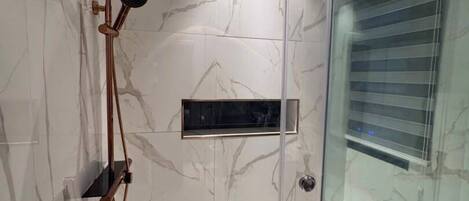 A modern shower enclosure with a glass door, a handheld showerhead, and a wall-mounted control panel.