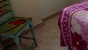 Una habitación con una silla verde, una cama con colcha floral morada y una estantería con un objeto rosa.