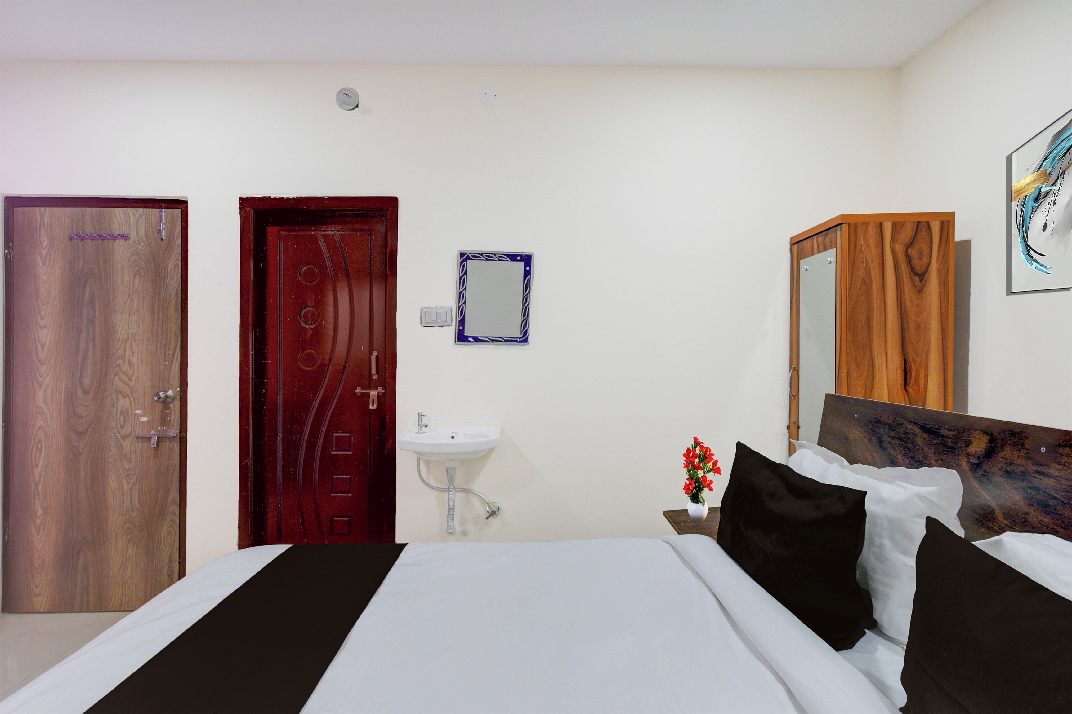 Een hotelkamer met een bed, een nachtkastje met een bloevas, een spiegel en een houten kledingkast.