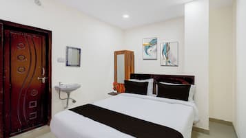 A hotel room with a bed, a wooden door, a wall-mounted sink, and two wall art pieces.
