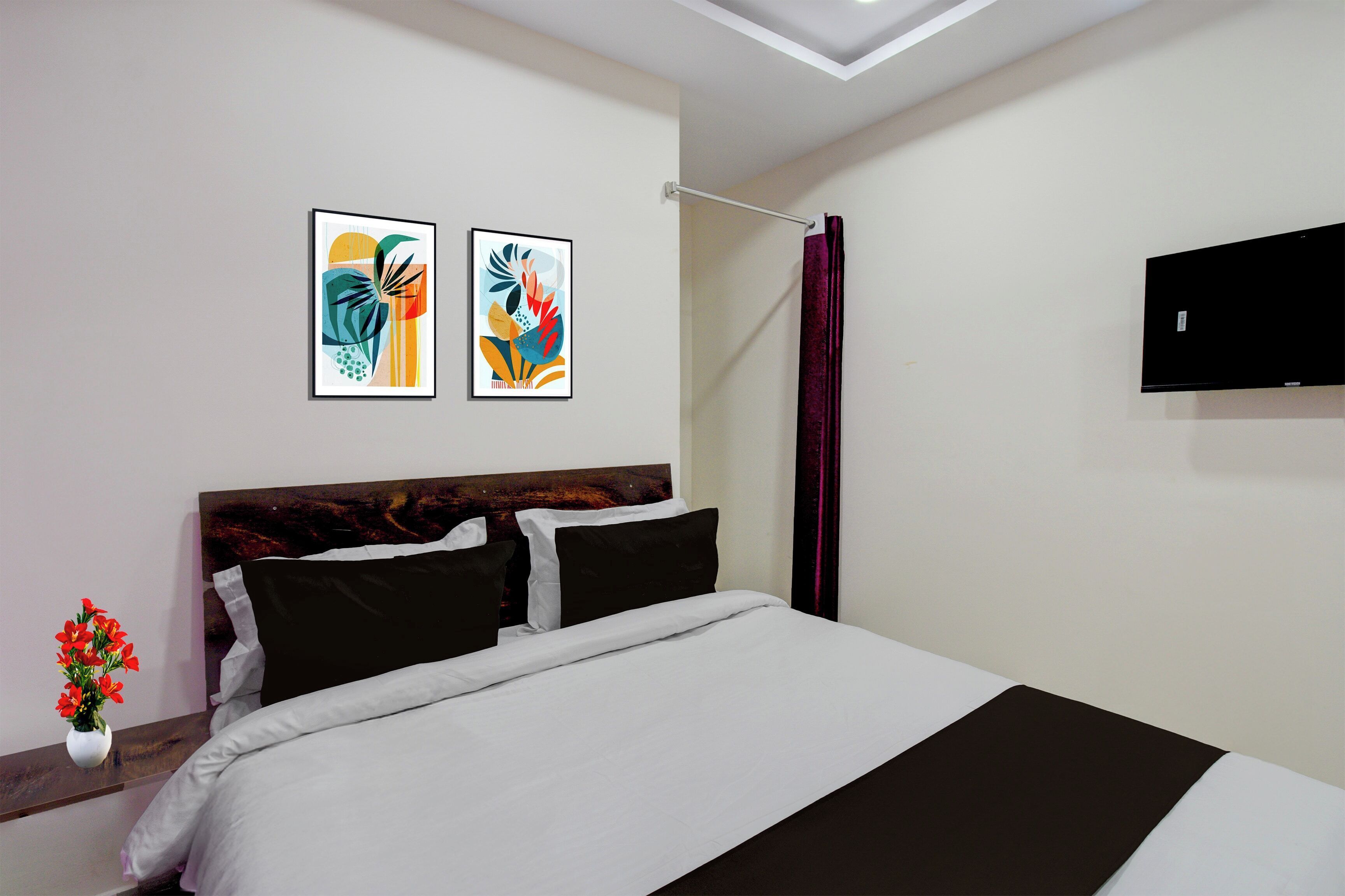 Une chambre d’hôtel avec un lit, deux œuvres d’art encadrées, un téléviseur à écran plat et un vase rempli de fleurs.
