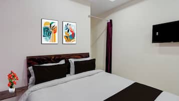 Une chambre d’hôtel avec un lit, deux œuvres d’art encadrées, un téléviseur à écran plat et un vase rempli de fleurs.