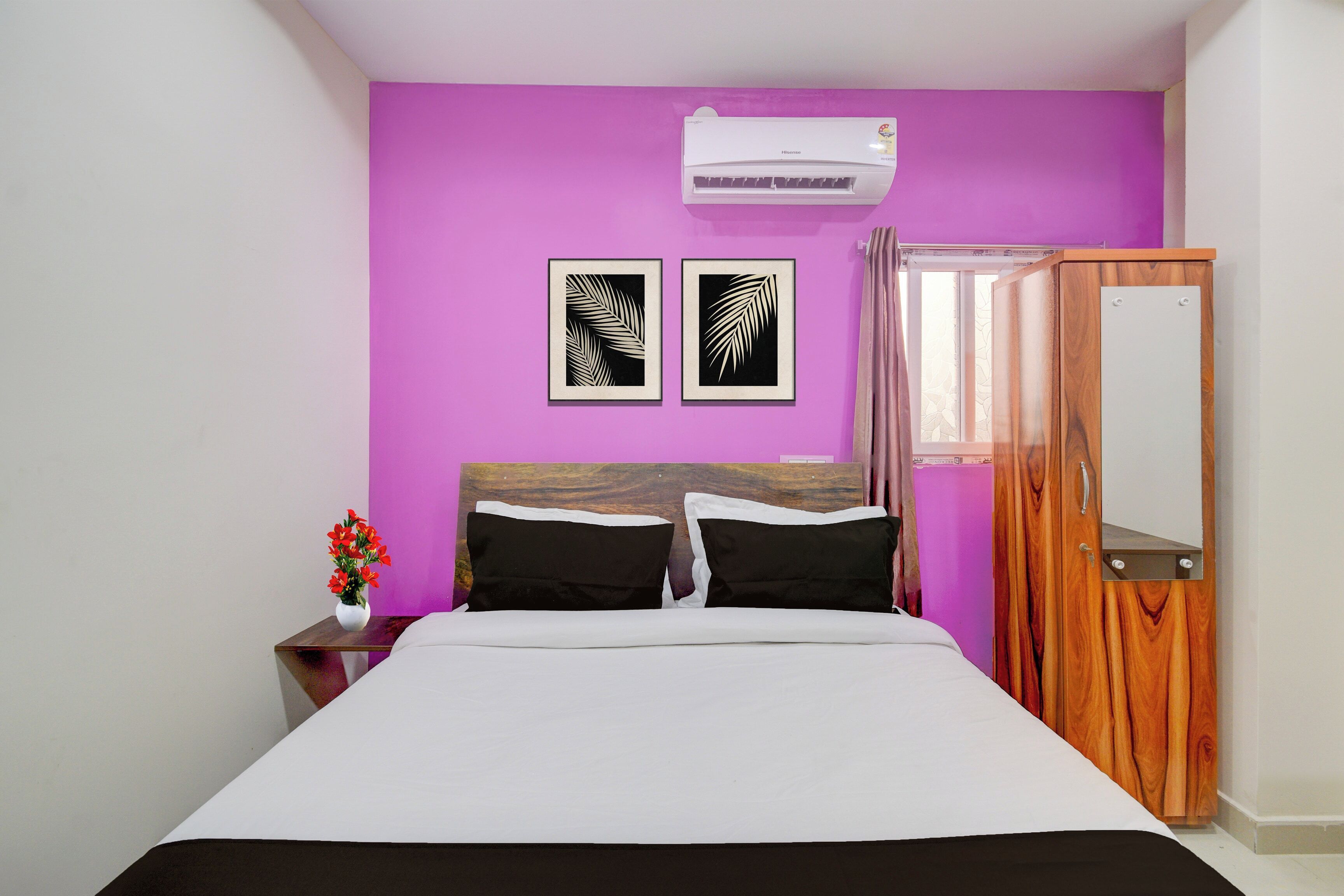 A bedroom with a bed, two wall-mounted air conditioning units, a wooden wardrobe, and two framed leaf designs on the wall.