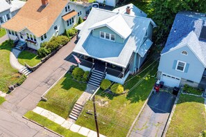 A residential area with houses featuring gabled roofs, a central house with a front porch, and a driveway. - Convenient, Cozy Home: Porches, Fire Pit, Office (Meriden)