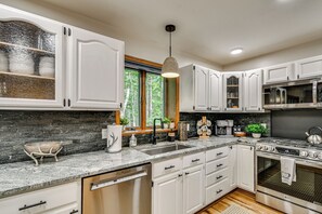 A modern kitchen with white cabinetry, granite countertops, a stainless steel dishwasher, and a built-in oven. - 'The Blue Goose Chalet': Your Cozy Up North Escape (Gaylord)