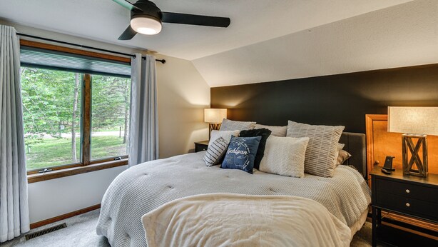 Een slaapkamer met een bed, nachtkastjes, een lamp, een plafondventilator en een raam met gordijnen.
